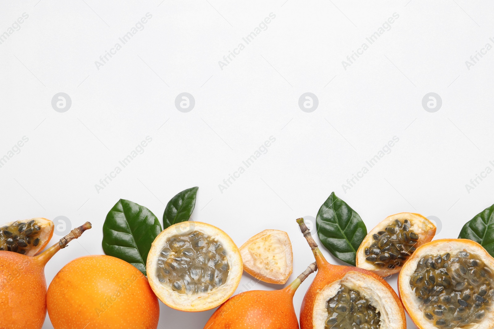 Photo of Delicious ripe granadillas with leaves on white background, flat lay. Space for text