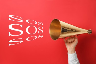 Woman holding retro megaphone and words SOS on color background. Asking for help