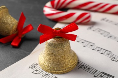 Photo of Golden shiny bell with red bow, music sheets and candy cane on grey table, closeup. Christmas decoration
