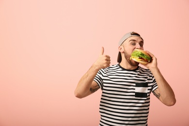 Photo of Young man eating tasty burger on color background. Space for text