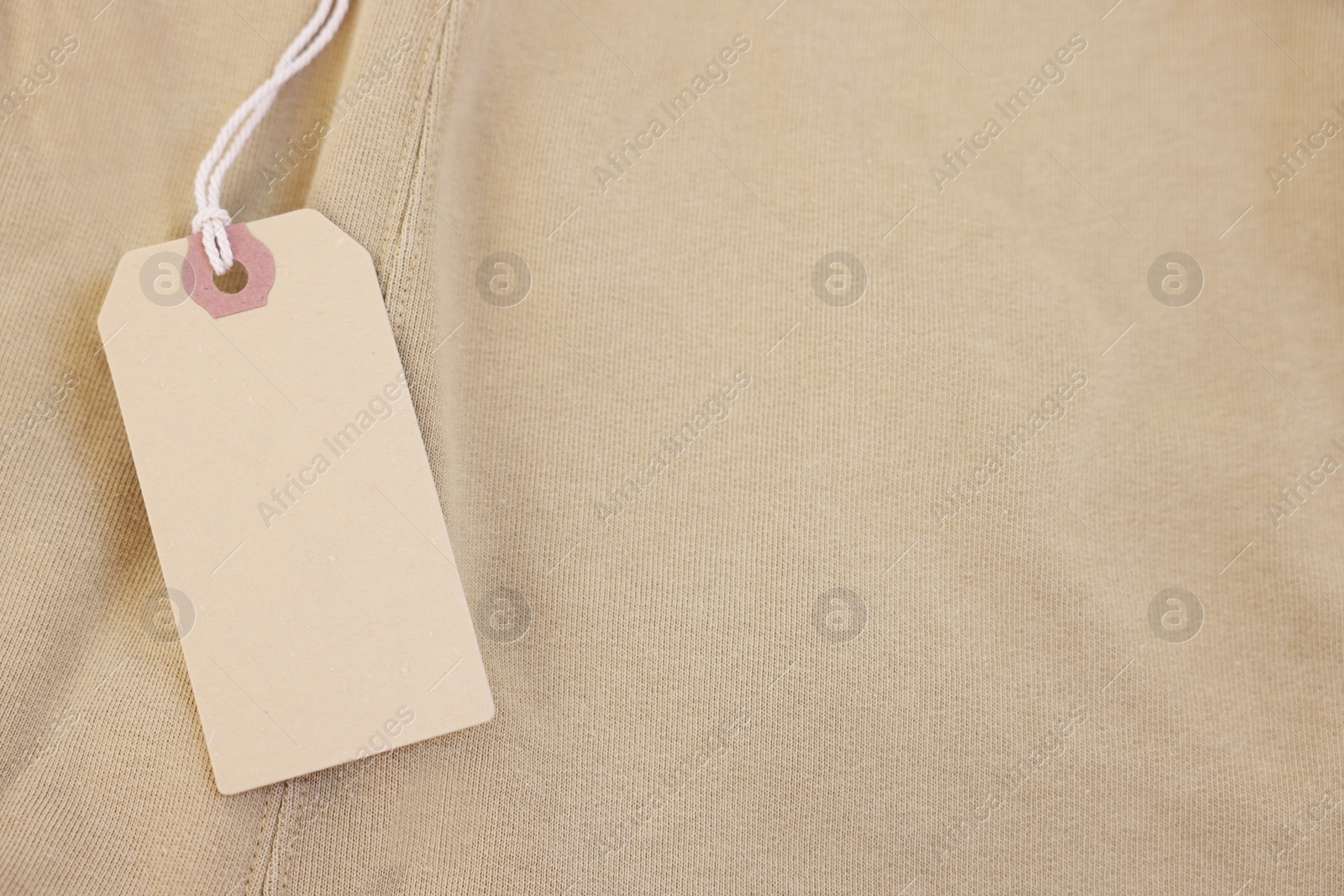 Photo of Cardboard tag on beige garment, top view. Space for text