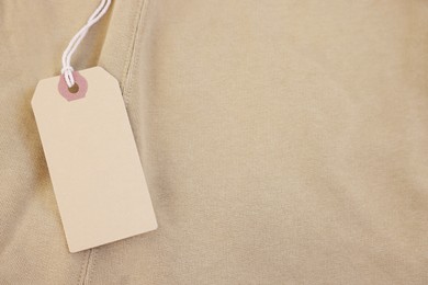 Photo of Cardboard tag on beige garment, top view. Space for text