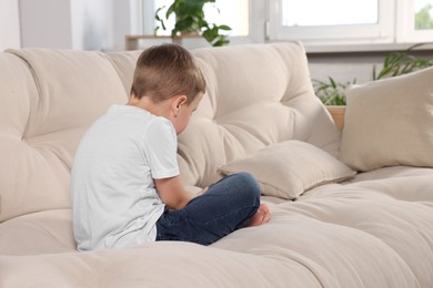 Boy with poor posture using phone on beige sofa in room. Symptom of scoliosis