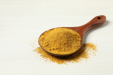 Photo of Curry powder in spoon on white wooden table. Space for text
