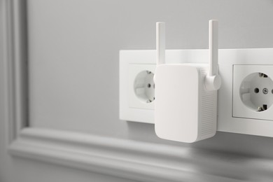 Photo of Wireless Wi-Fi repeater on light grey wall indoors, space for text