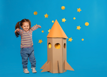 Photo of Little child playing with rocket made of cardboard box near stars on blue background