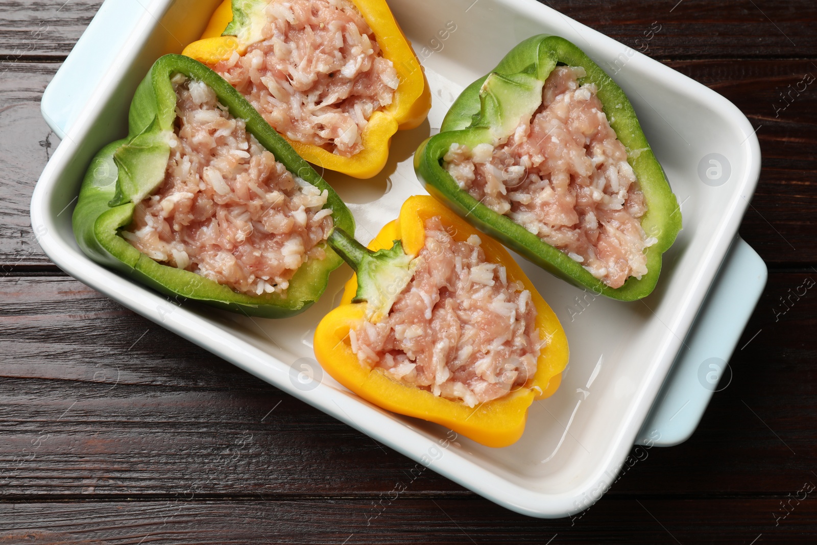 Photo of Raw stuffed peppers in dish on wooden table, top view