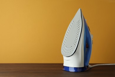 One modern iron on wooden table against orange background, space for text. Home appliance