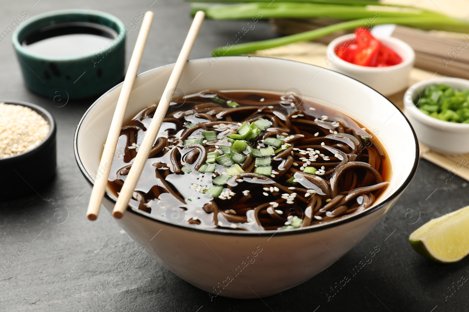 Photo of Tasty soup with buckwheat noodles (soba) and onion in bowl served on grey table, closeup