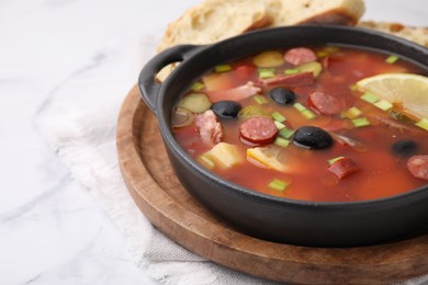 Photo of Meat solyanka soup with thin dry smoked sausages in bowl on white marble table, closeup. Space for text