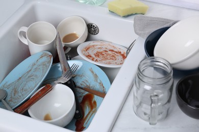 Photo of Sink with many dirty utensils and dishware on countertop in messy kitchen