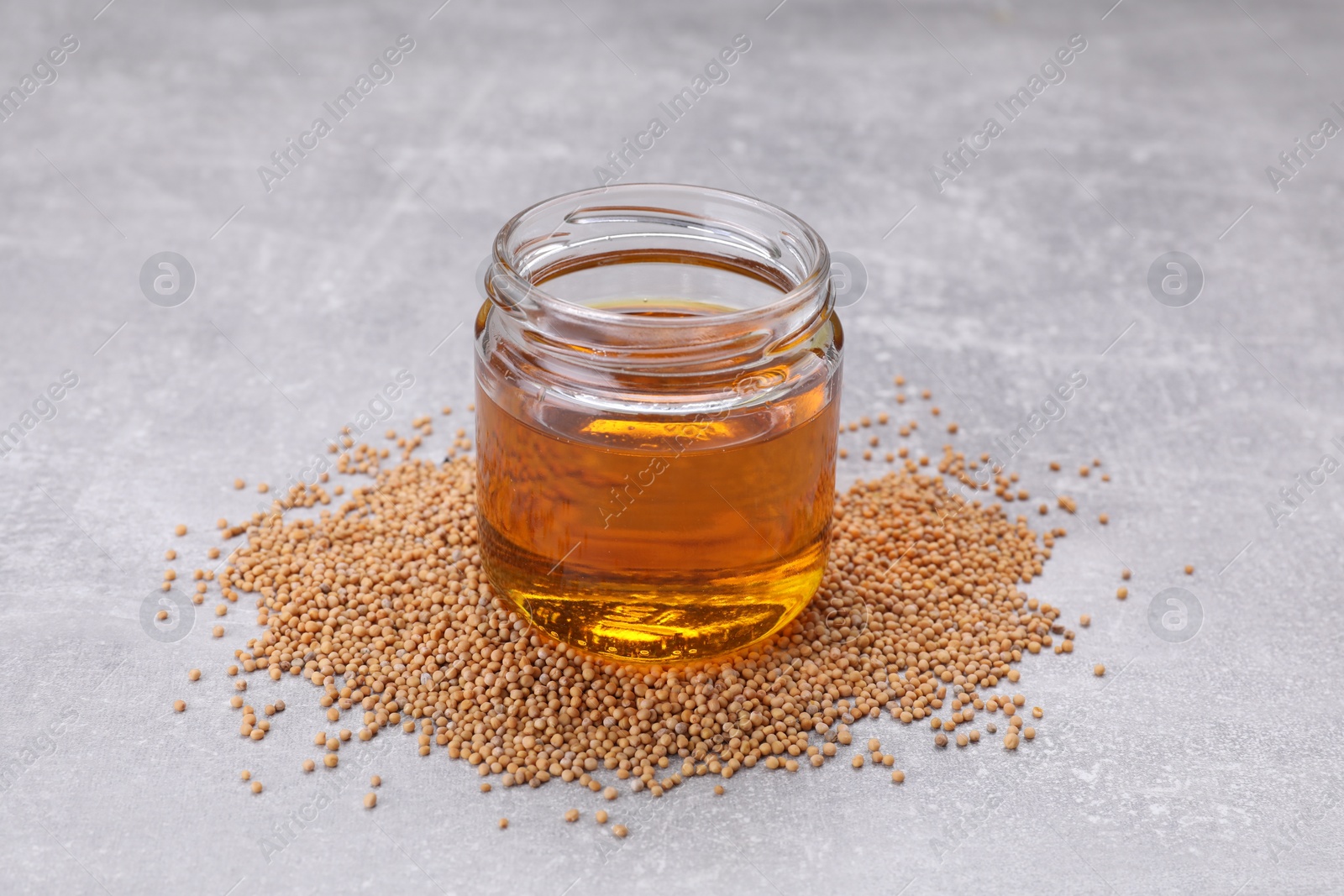 Jar of natural oil and mustard seeds on light grey table Photo of Jar of natural oil and mustard seeds on light grey table