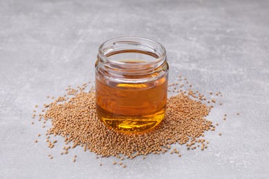 Photo of Jar of natural oil and mustard seeds on light grey table