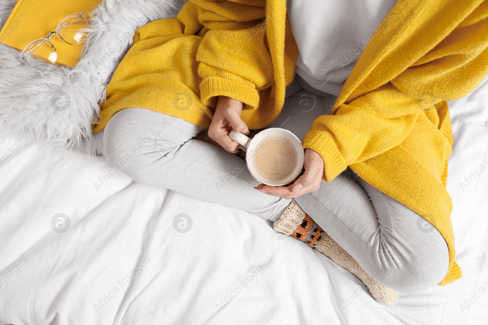 Photo of Woman with coffee wearing knitted socks on white fabric, top view. Warm clothes
