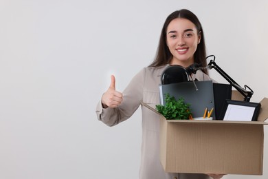 Photo of Happy unemployed woman with box of personal office belongings showing thumbs up on white background, space for text