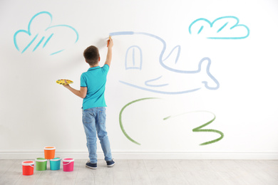 Image of Little child drawing plane on white wall indoors