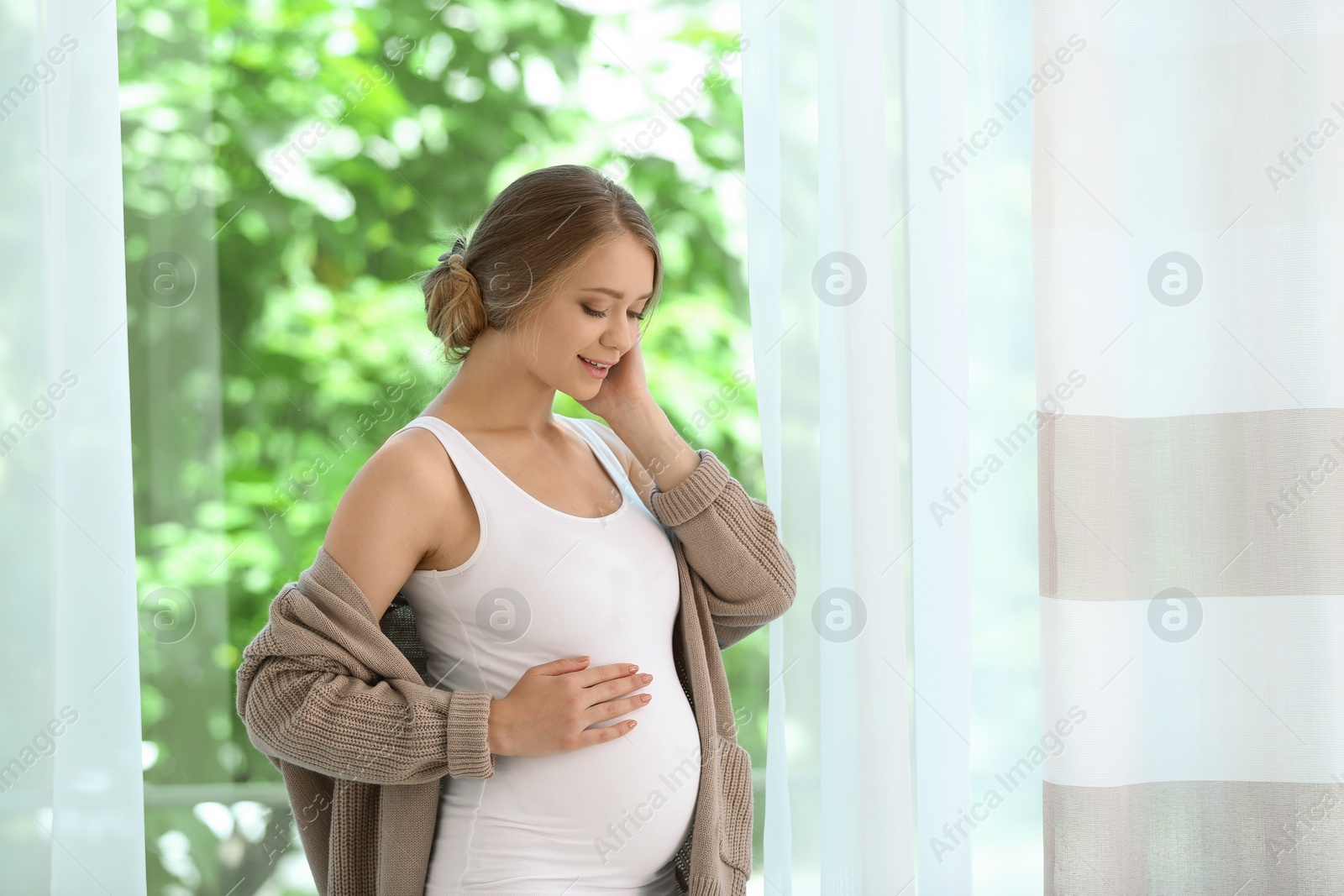 Photo of Happy pregnant woman standing near window at home