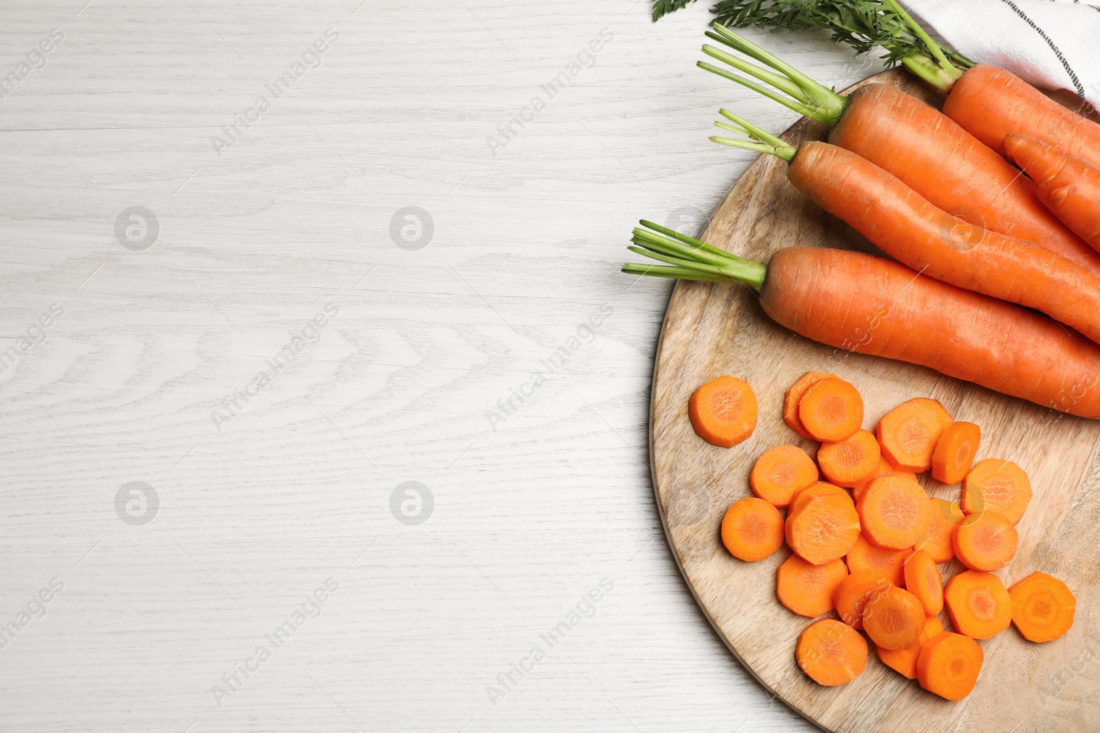 Photo of Whole and sliced fresh ripe juicy carrots on white wooden table, top view. Space for text