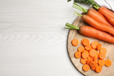 Photo of Whole and sliced fresh ripe juicy carrots on white wooden table, top view. Space for text