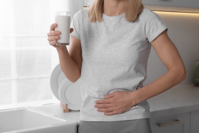 Woman with glass of milk suffering from lactose intolerance in kitchen, closeup