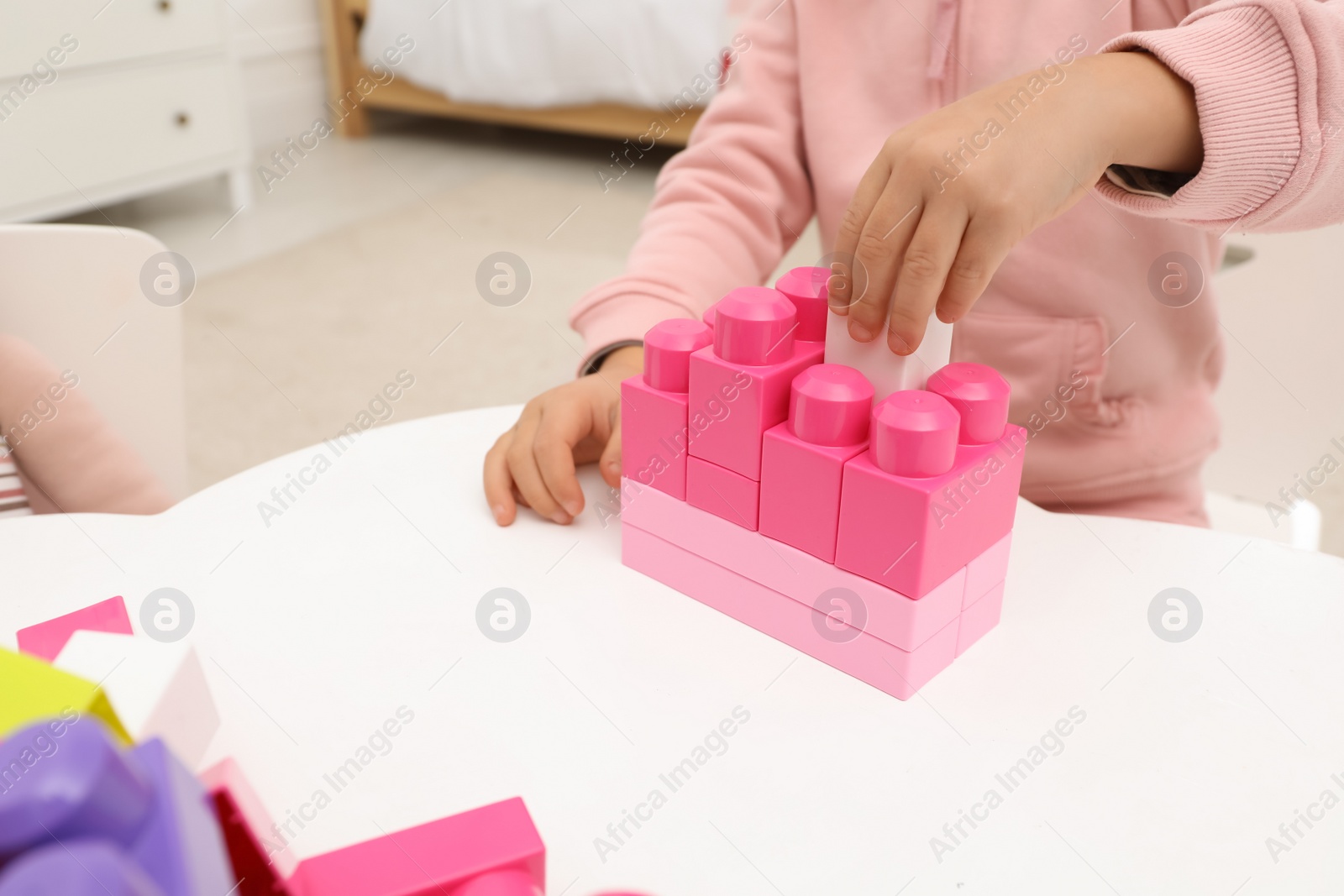 Photo of Cute little girl playing with colorful building blocks at table indoors, closeup. Space for text