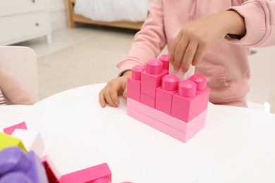 Cute little girl playing with colorful building blocks at table indoors, closeup. Space for text