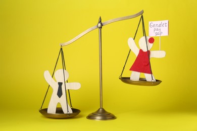 Photo of Gender pay gap. Wooden figures of man and woman on scales against yellow background