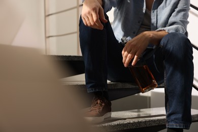 Photo of Addicted man with alcoholic drink on stairs indoors, closeup. Space for text