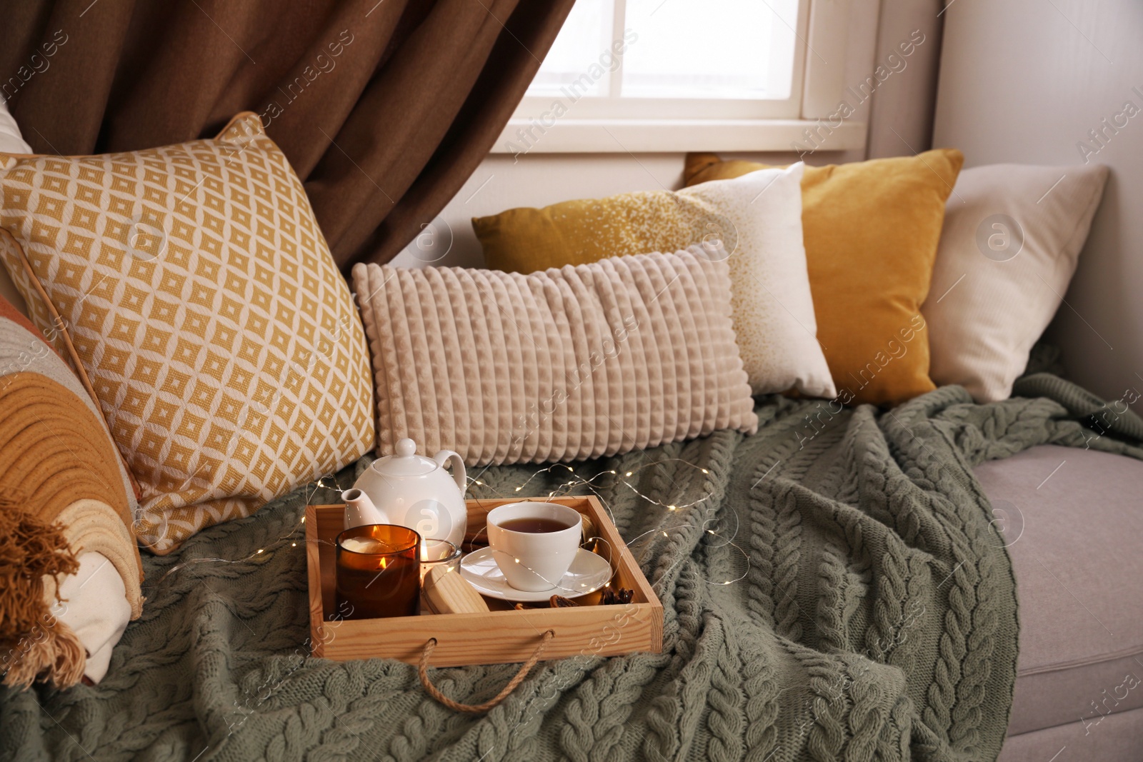 Photo of Comfortable lounge area with knitted blanket and soft pillows near window in room