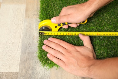 Man cutting artificial grass carpet indoors, closeup. Space for text