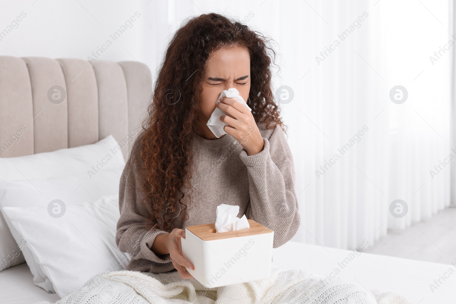 Photo of Sick African American woman with box of paper tissues suffering from cold in bed at home