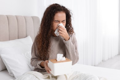 Sick African American woman with box of paper tissues suffering from cold in bed at home