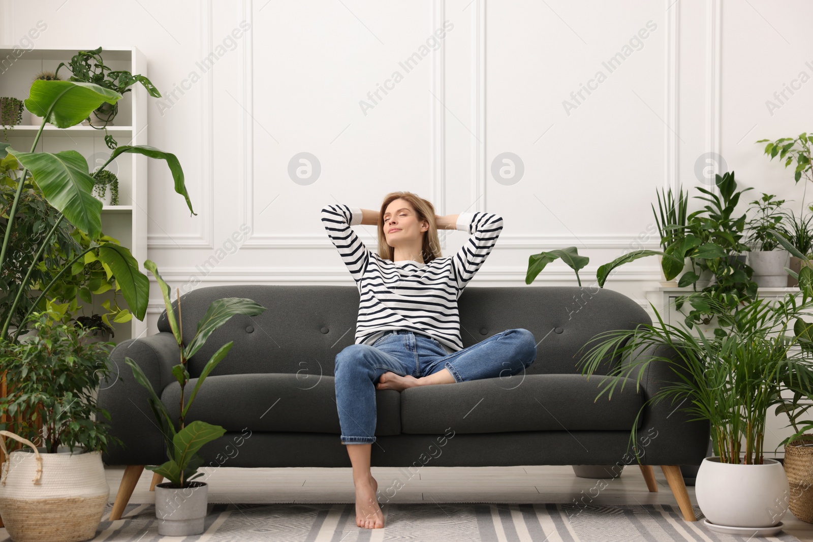 Photo of Woman relaxing on sofa surrounded by beautiful potted houseplants at home