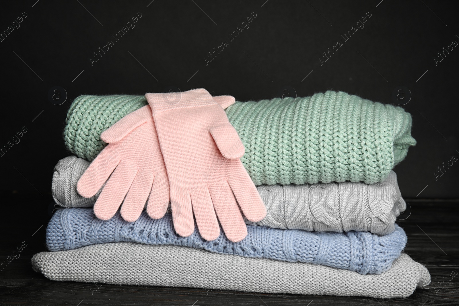 Photo of Stacked sweaters and gloves on table, closeup. Autumn clothes