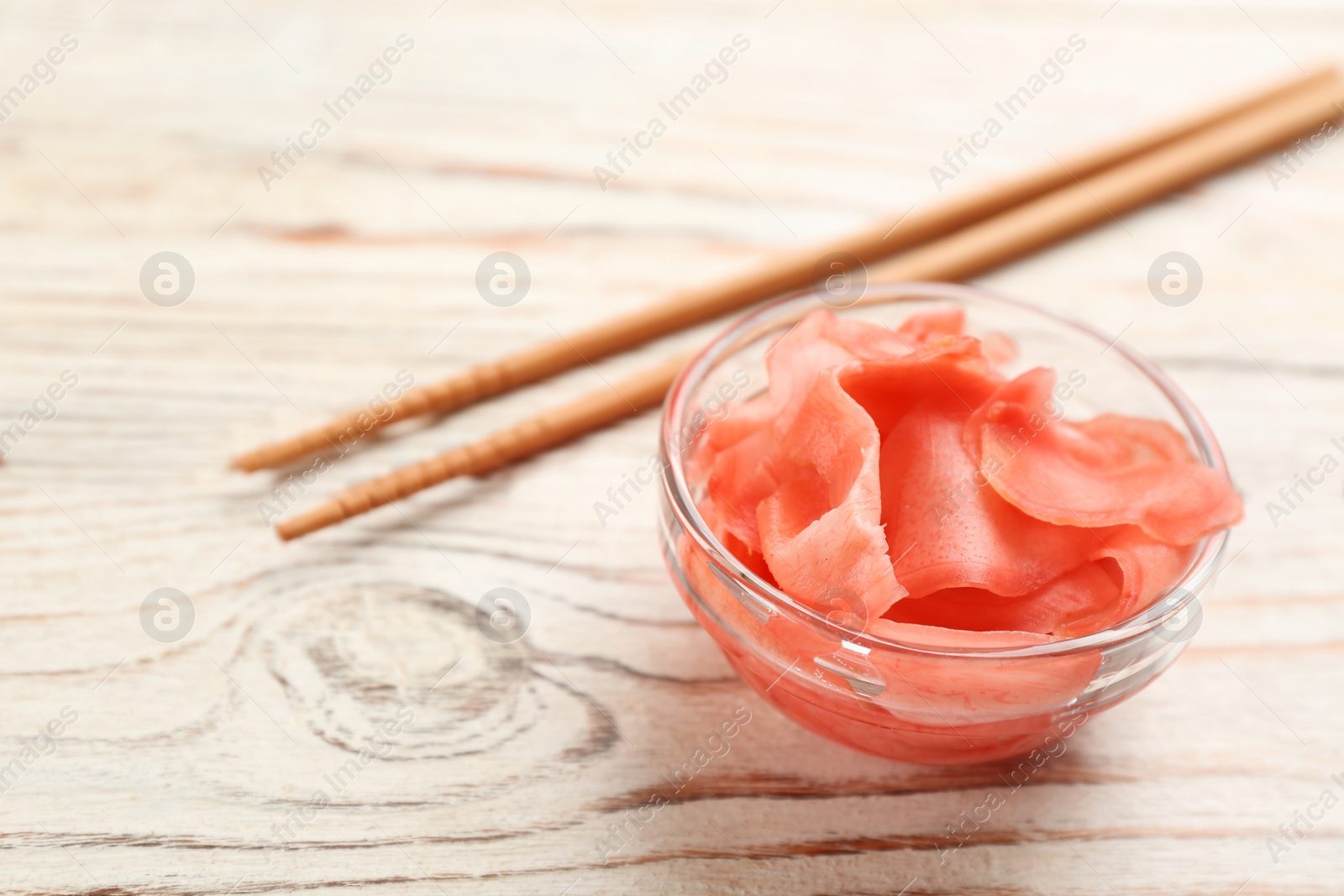 Photo of Spicy pickled ginger and chopsticks on white wooden table, closeup. Space for text