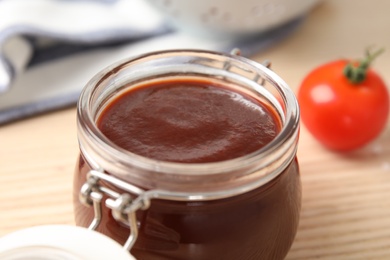 Photo of Glass jar of hot barbecue sauce on table, closeup