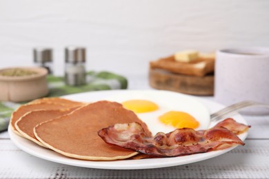 Tasty pancakes served with fried eggs and bacon on white wooden table, closeup