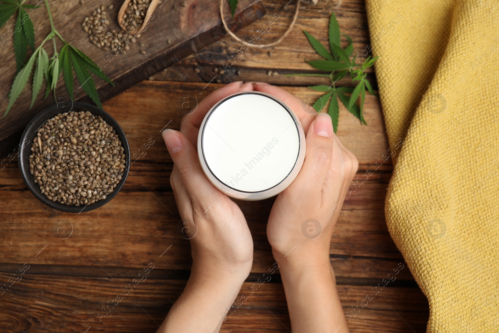 Photo of Woman with glass of hemp milk at wooden table, top view