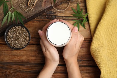 Photo of Woman with glass of hemp milk at wooden table, top view