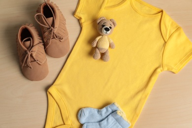 Baby onesie, shoes, socks and toy bear on wooden table, flat lay