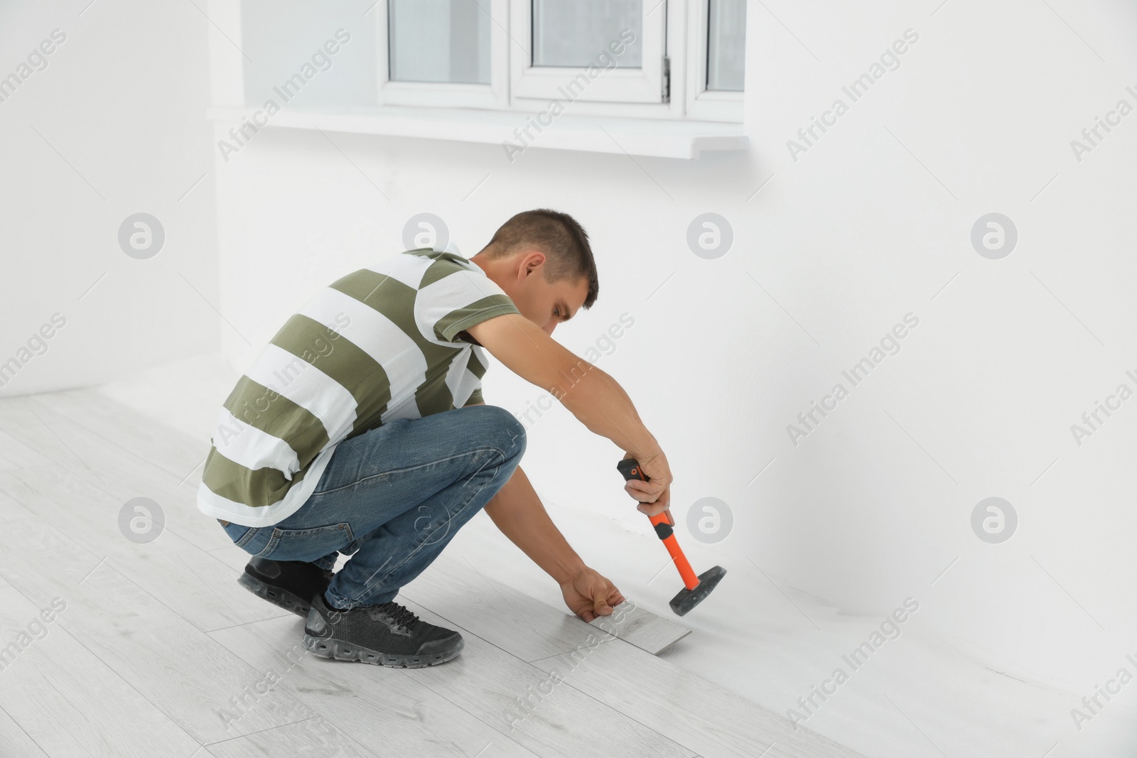 Photo of Professional worker using hammer during installation of new laminate flooring indoors