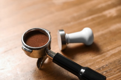 Photo of Portafilter with milled coffee and tamper on wooden table, closeup. Space for text