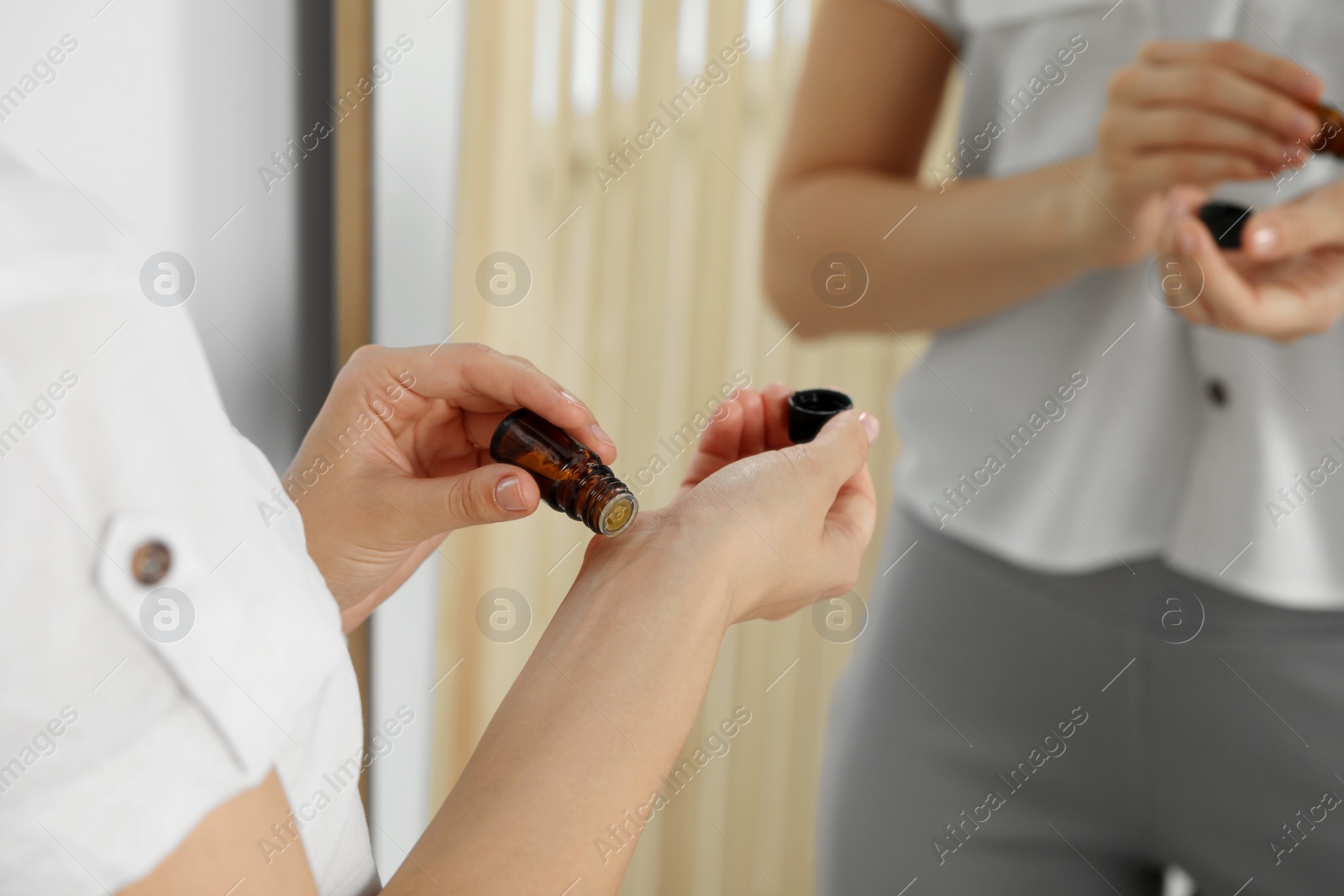 Photo of Young woman applying essential oil onto wrist indoors, closeup