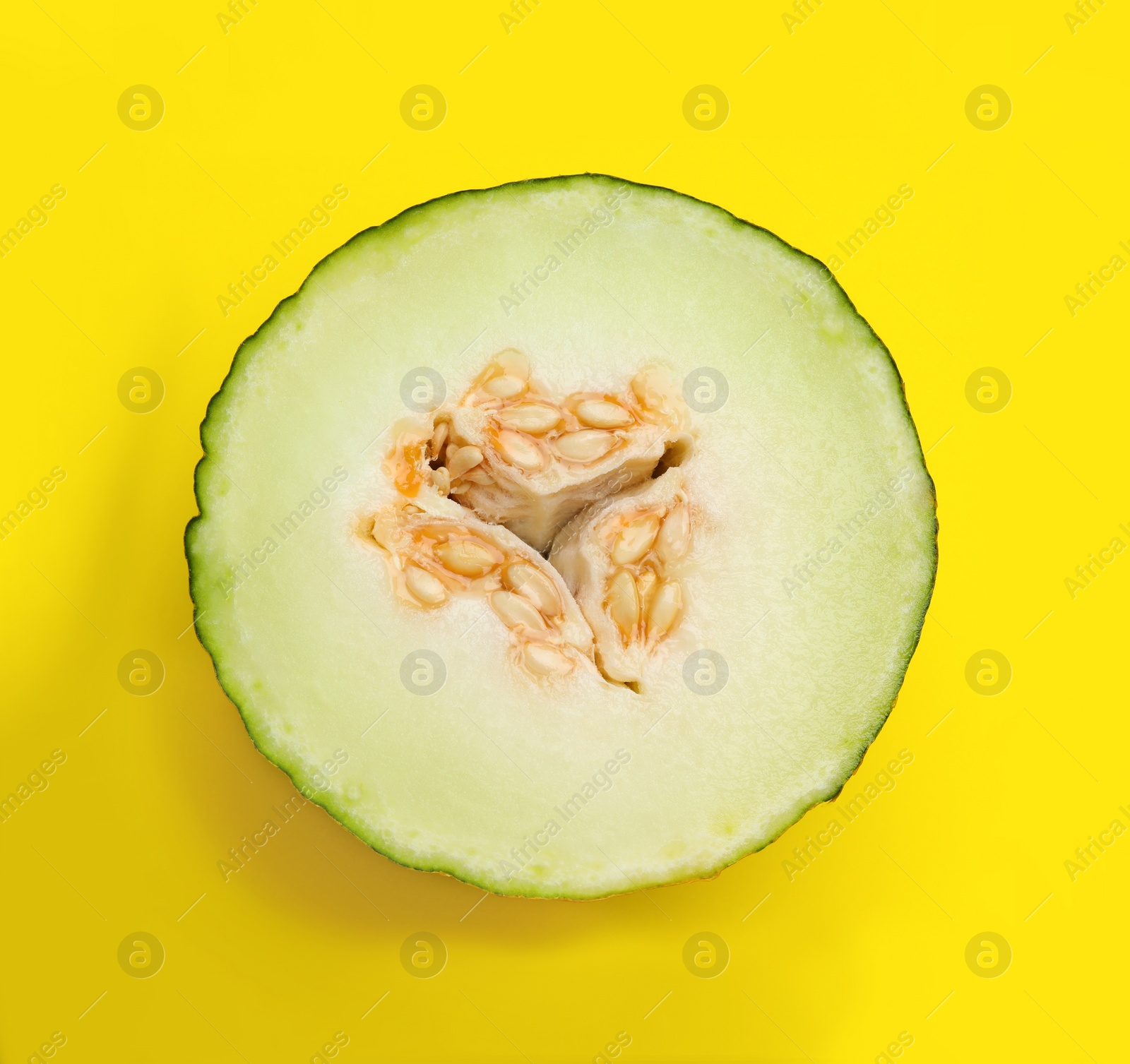 Photo of Half of ripe tasty melon on yellow background, top view