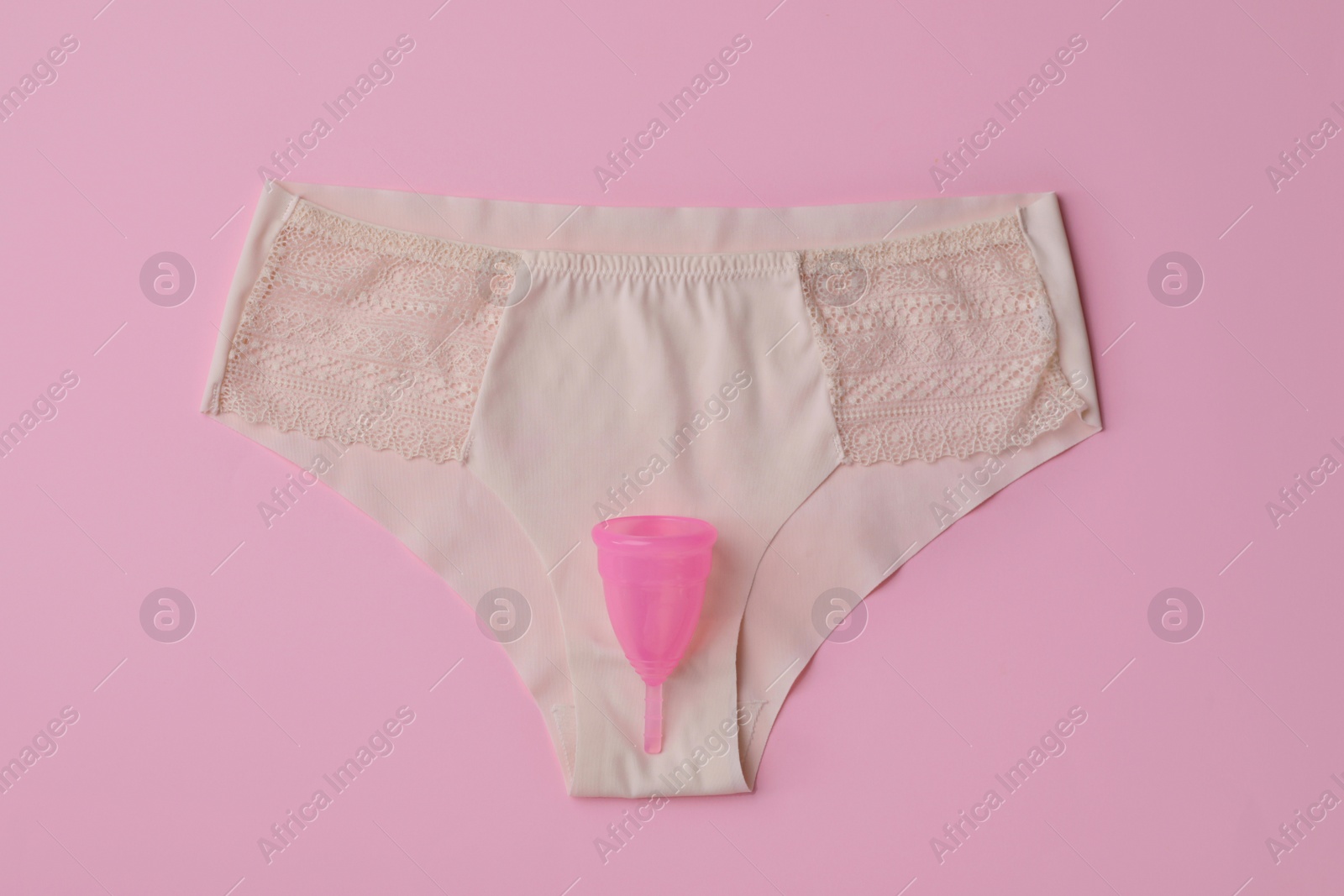 Photo of Panties and menstrual cup on pink background, top view