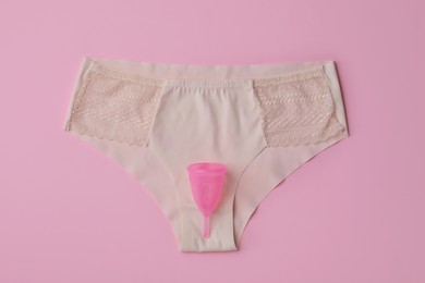 Photo of Panties and menstrual cup on pink background, top view
