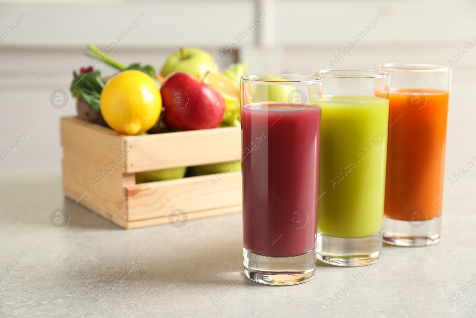 Photo of Three glasses of different juices and wooden crate with fresh ingredients on light table