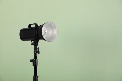 Photo of Studio flash light with reflector against pale green background, space for text. Professional photographer's equipment