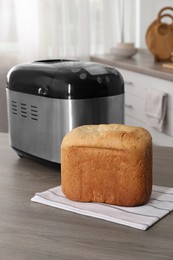 Photo of Breadmaker and fresh homemade bread on wooden table in kitchen