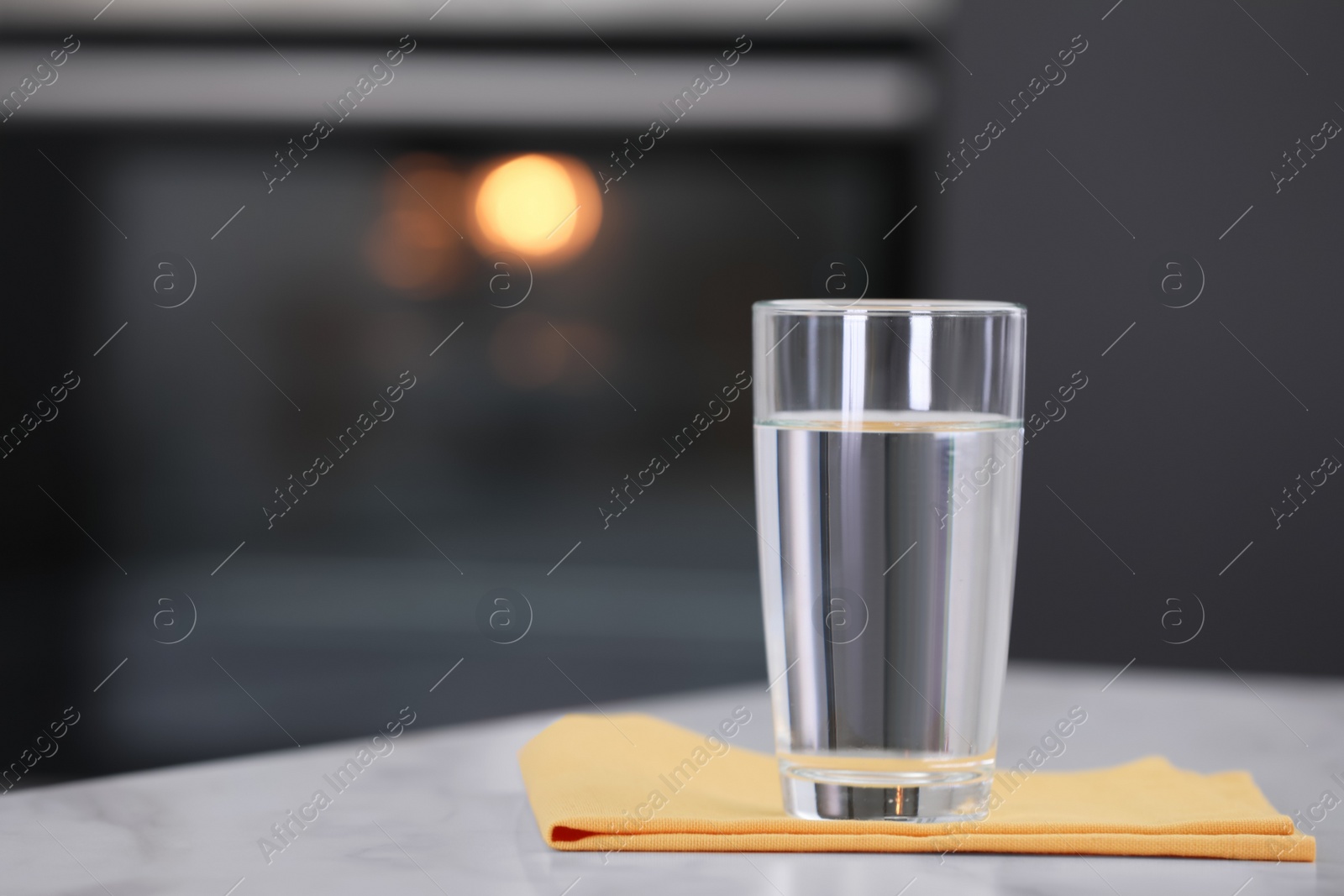 Photo of Glass of water and napkin on white table against blurred background. Space for text